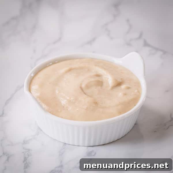 A small bowl of creamy tahini dip, garnished with fresh herbs and a drizzle of olive oil, accompanied by fresh vegetable sticks.