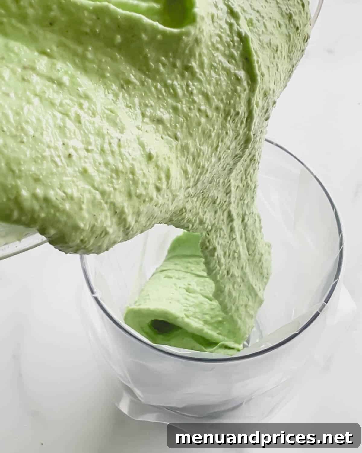 Minty Cocoa Macaron Bliss 11 Vibrant green macaron batter is being carefully poured into a piping bag, which is neatly fitted into a glass for easy filling.