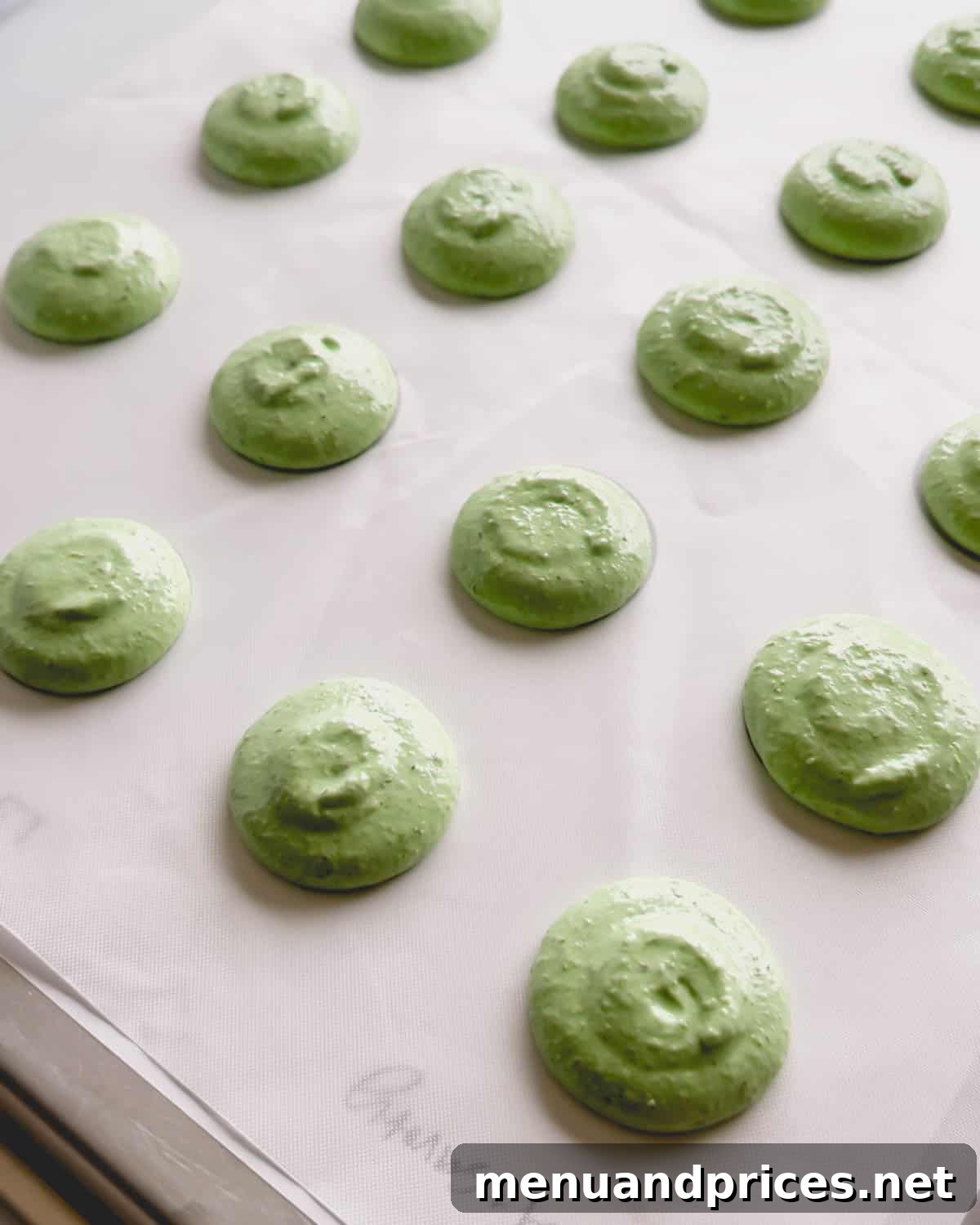 Minty Cocoa Macaron Bliss 13 Unbaked vibrant green macaron shells, perfectly piped and resting on a white surface, patiently waiting for their turn in the oven.