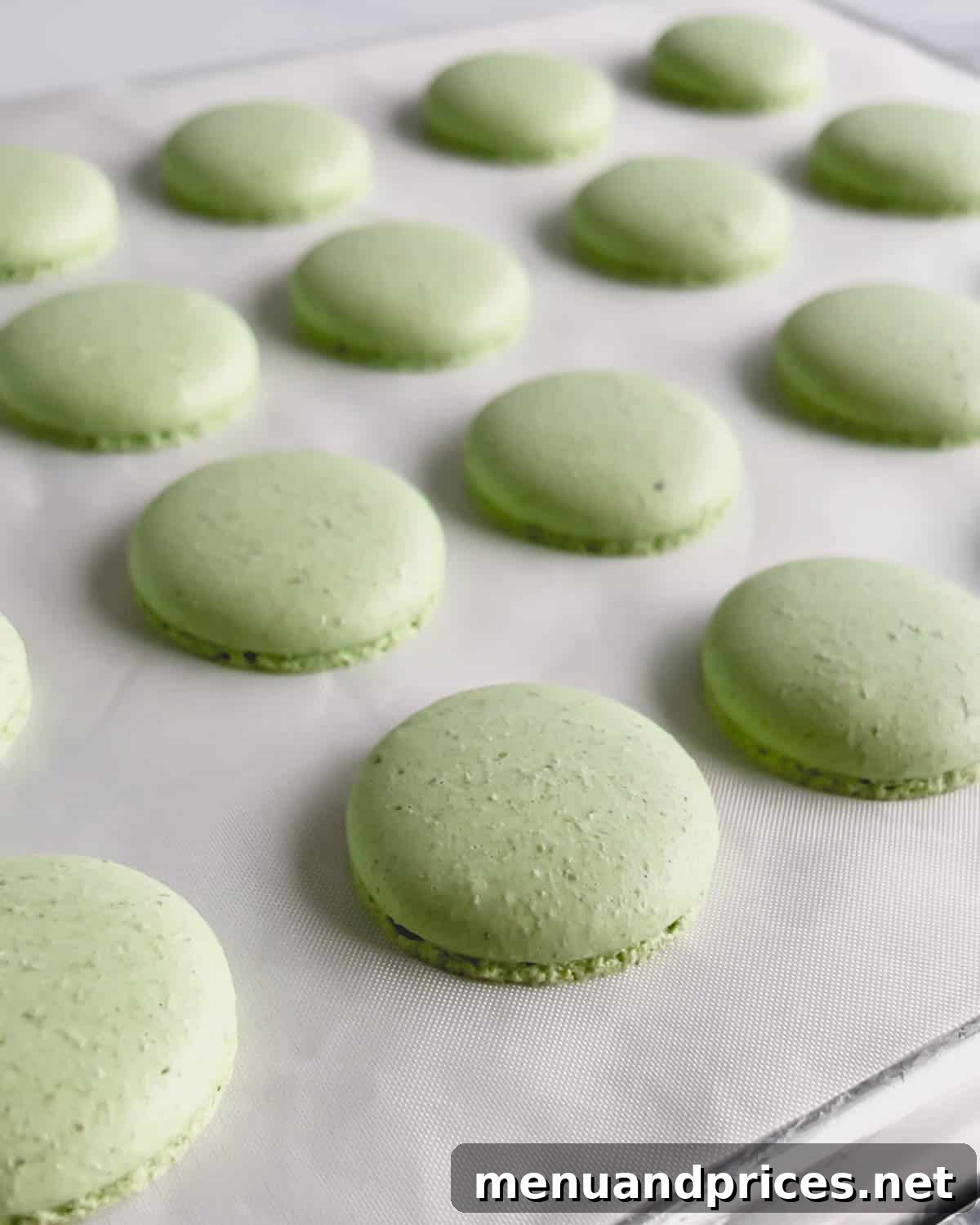 Minty Cocoa Macaron Bliss 14 A freshly baked batch of vibrant green macaron shells, now with perfect 'feet' and smooth tops, cooling on a white surface after their oven journey.