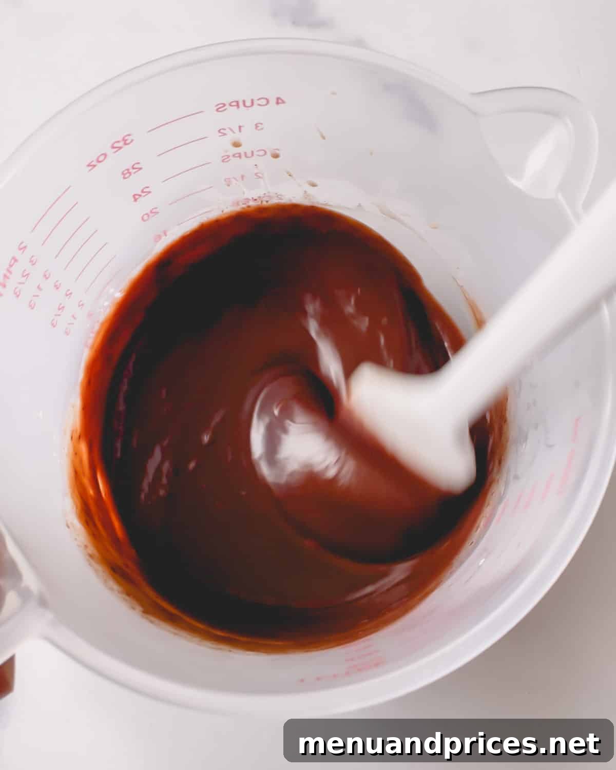 Minty Cocoa Macaron Bliss 15 Rich chocolate ganache is being expertly mixed with a spatula in a deep cup, achieving a smooth and luxurious consistency.