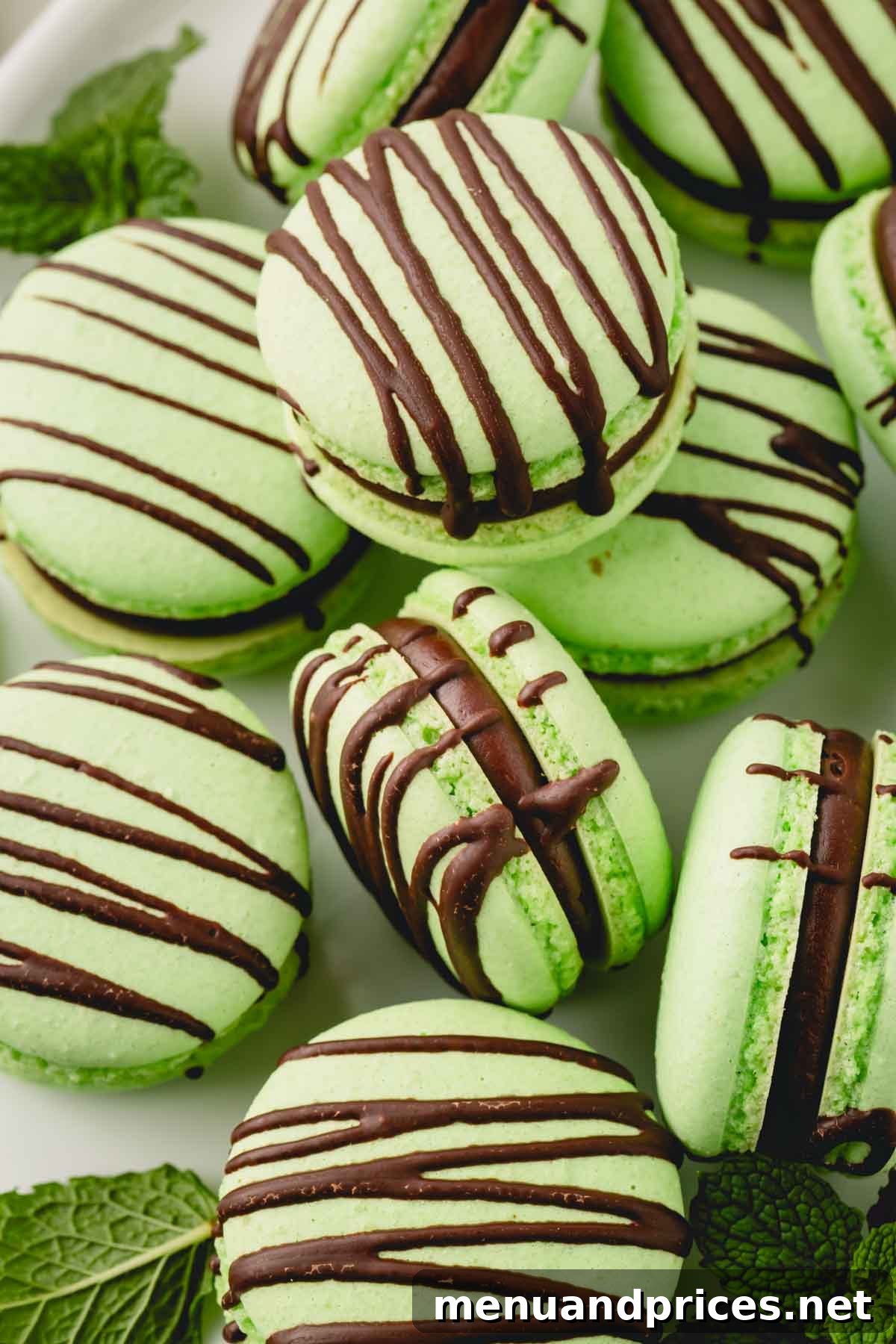 Minty Cocoa Macaron Bliss 3 Vibrantly green mint macarons, filled with dark mint ganache and delicately drizzled with chocolate, presented alongside fresh mint leaves for garnish.