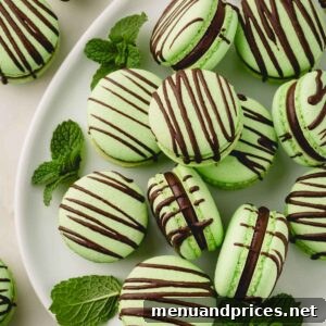 Green mint macarons filled with dark mint ganache and drizzled with chocolate arranged on a white oval plate and garnished with mint leaves.