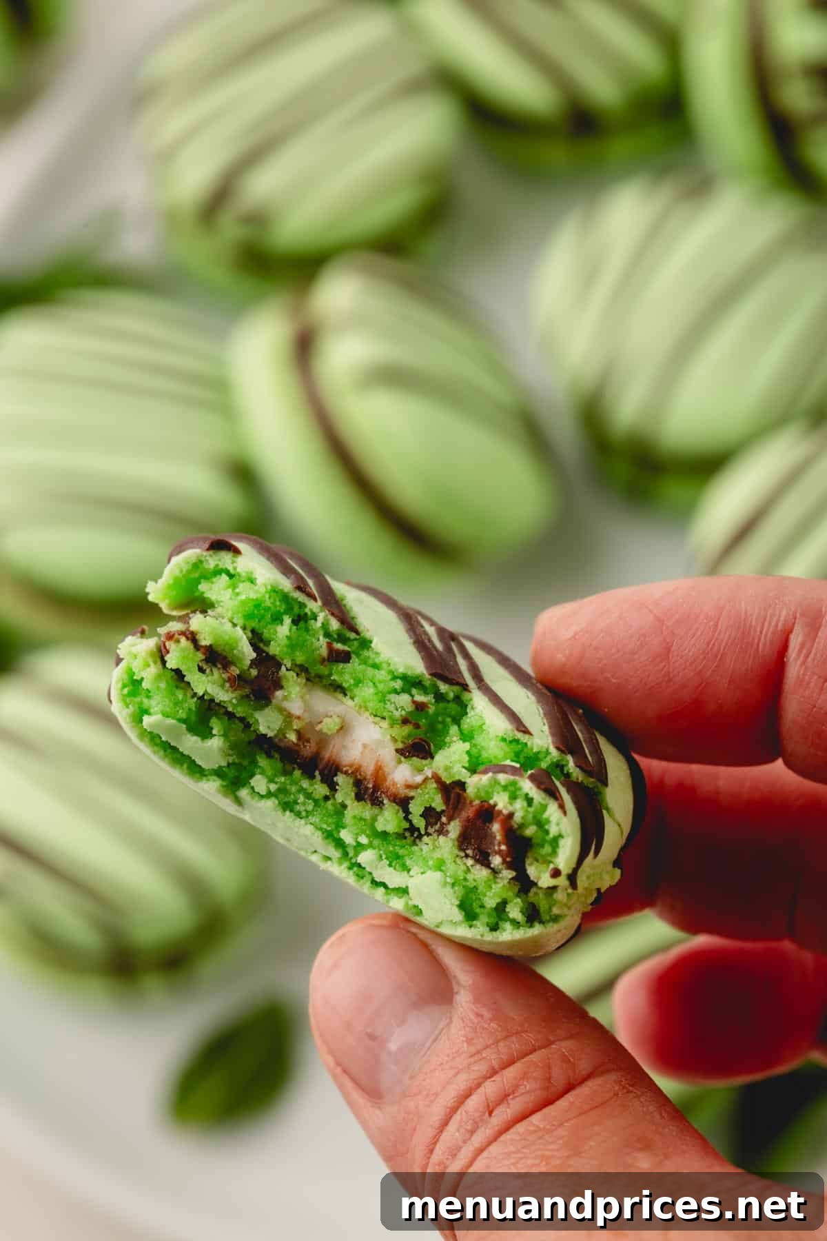 Minty Cocoa Macaron Bliss 4 A close-up of a green mint chocolate ganache macaron, with a bite taken to reveal the creamy white mint candy center.
