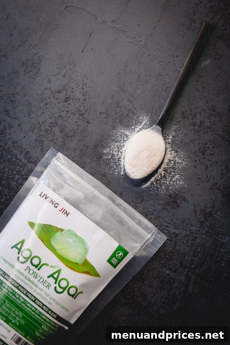 A packet of agar agar powder displayed next to a spoon filled with agar, all on a sleek black background.