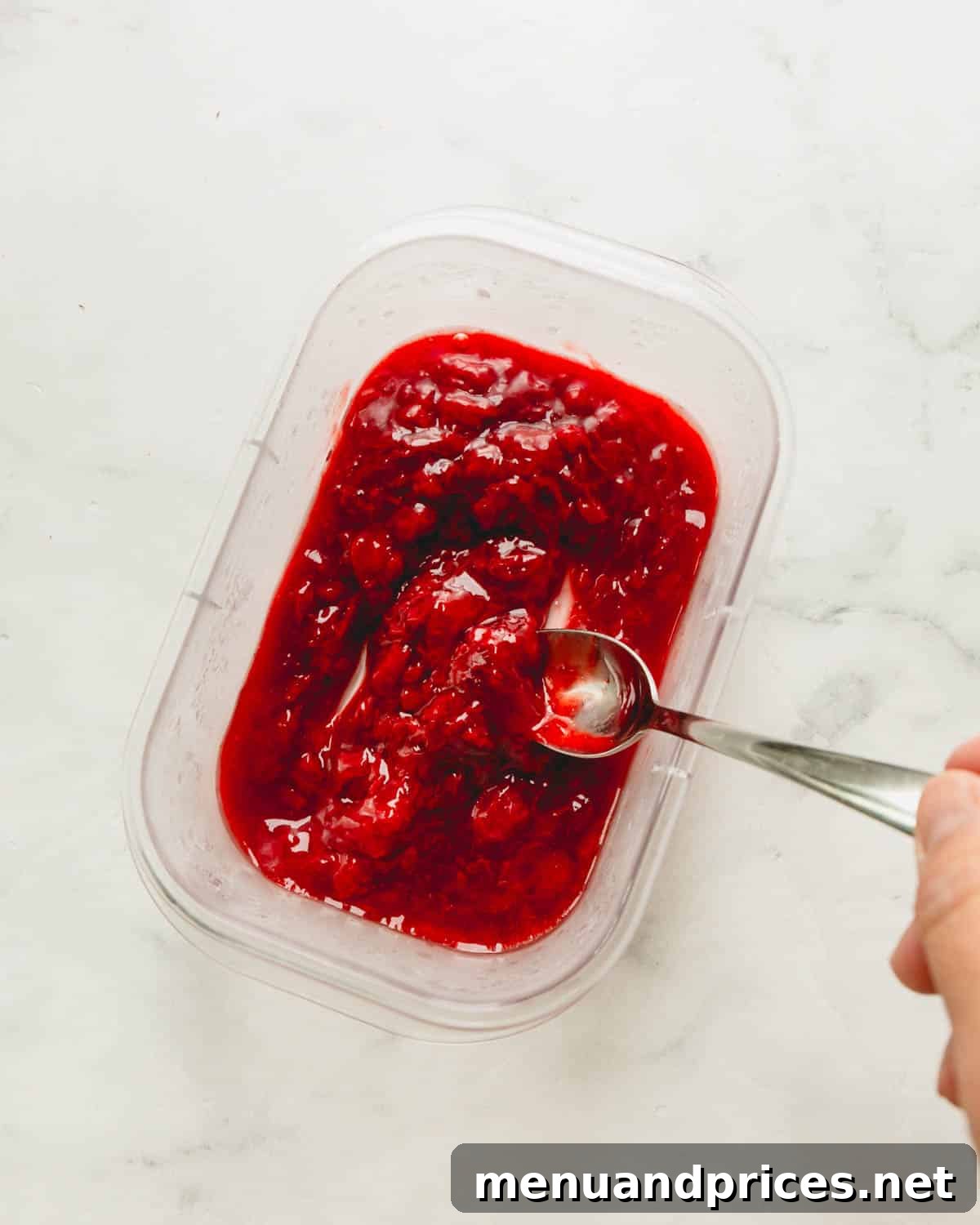 Thick, vibrant strawberry sauce shown in a clear container with a spoon resting inside, highlighting its smooth texture.