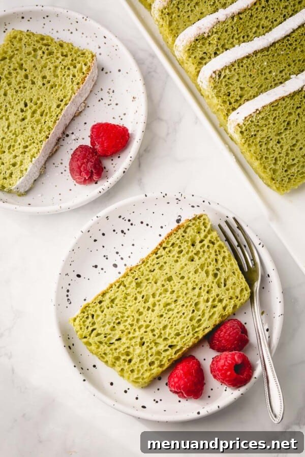 Beautifully presented matcha sponge cake slice, dusted with powdered sugar and adorned with fresh berries.