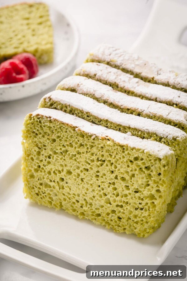 A slice of matcha sponge cake elegantly plated with fresh berries, a dusting of powdered sugar, and a delicate presentation.