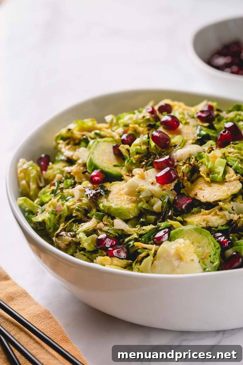 Brussels Sprout Ribbon Salad with Pomegranate 3 A close-up shot of a vibrant shaved Brussels sprouts salad, artfully garnished with bright red pomegranate arils, ready for serving.