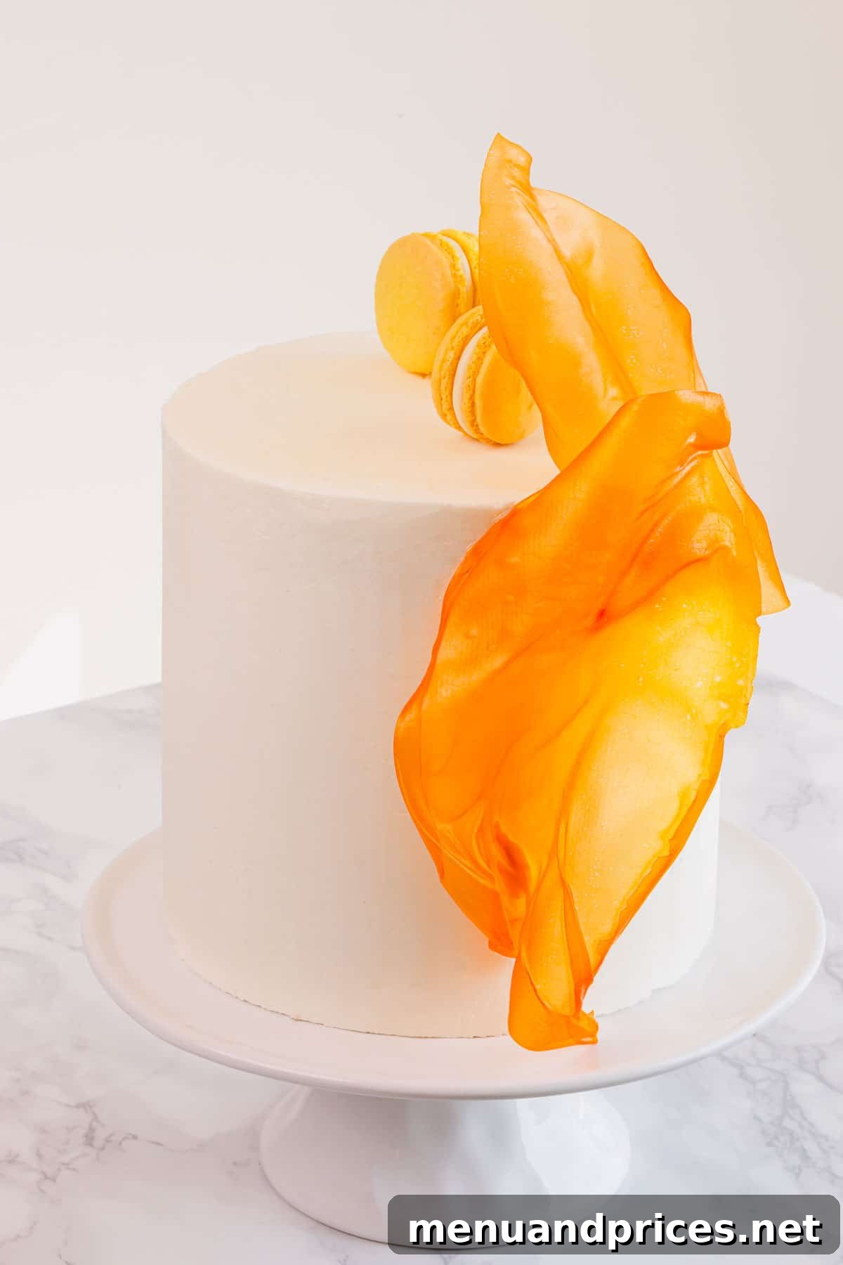 Crafting Elegant Rice Paper Sails for Cake Art 4 A tall, elegant white layer cake beautifully decorated with vibrant orange rice paper sails and delicate macarons, presented on a pristine cake stand.