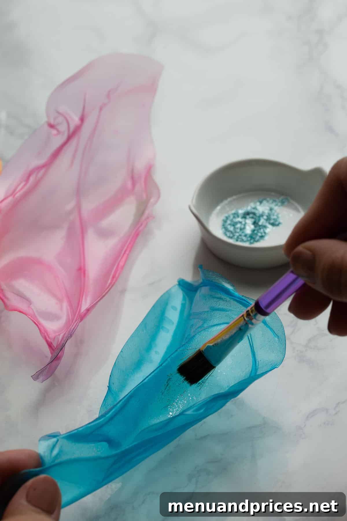 Crafting Elegant Rice Paper Sails for Cake Art 6 A close-up shot of a blue rice paper sail being meticulously painted with edible glitter, highlighting the process of adding shimmer and decorative accents.