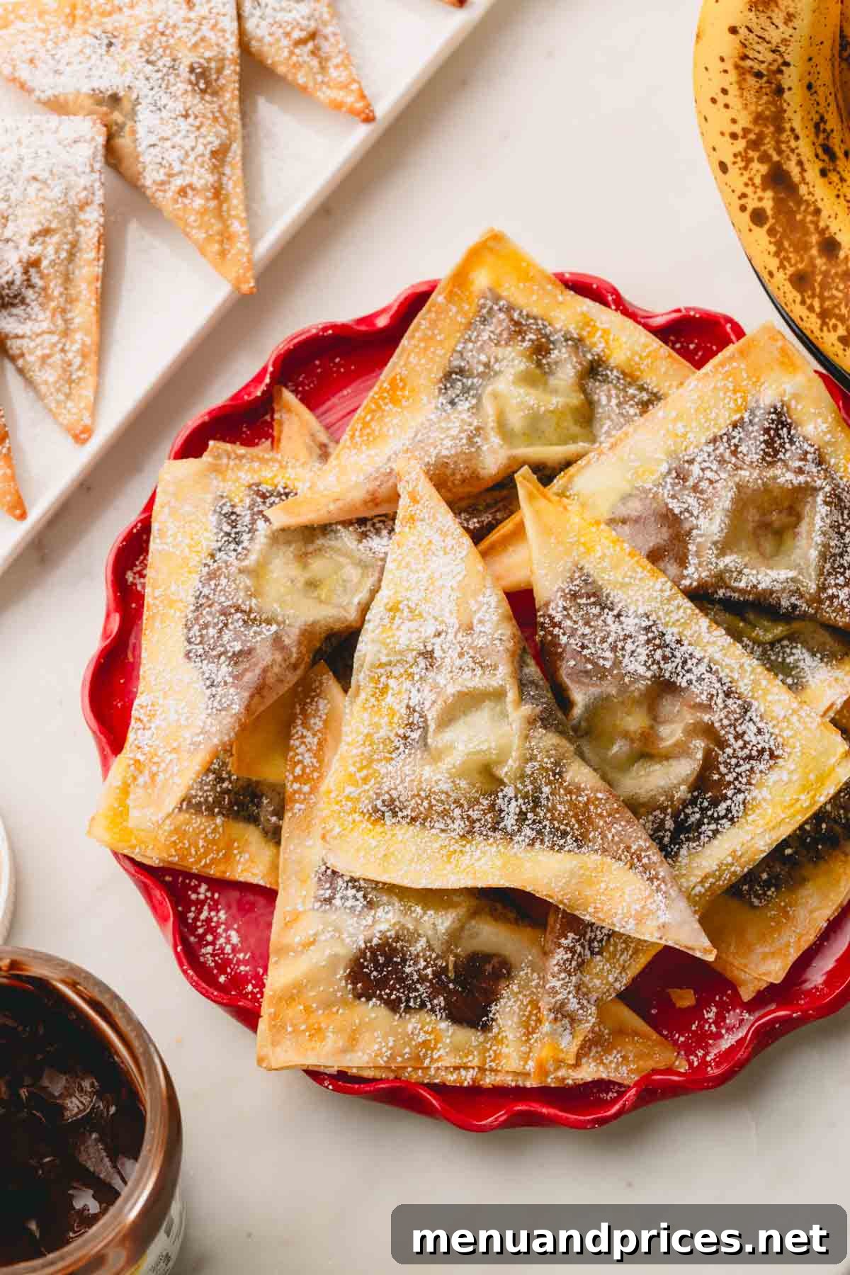 A plate of golden-brown banana Nutella wontons dusted with powdered sugar, ready to be served.