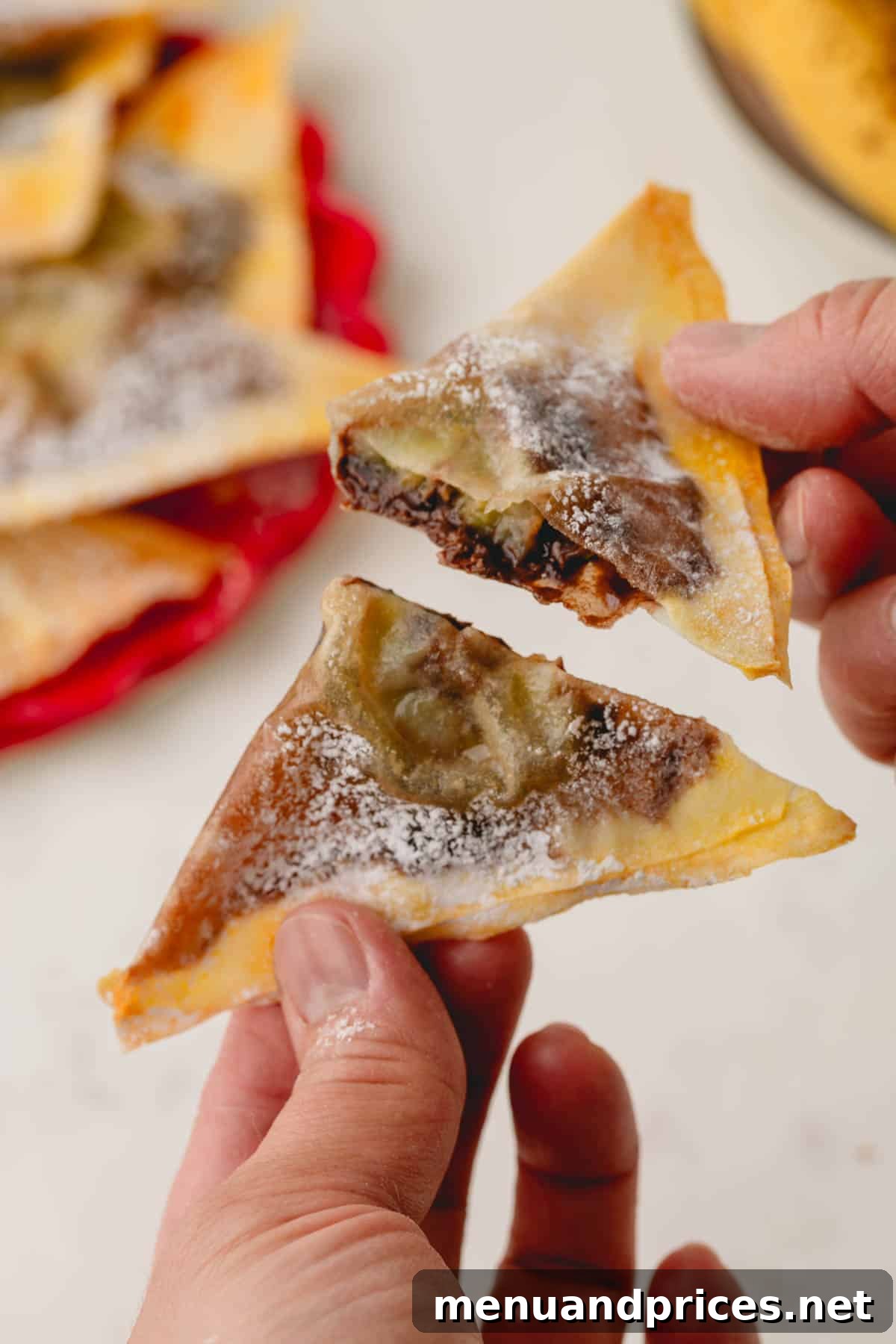 Two hands, each holding a half of a freshly baked banana Nutella wonton, showcasing the warm, melted filling.