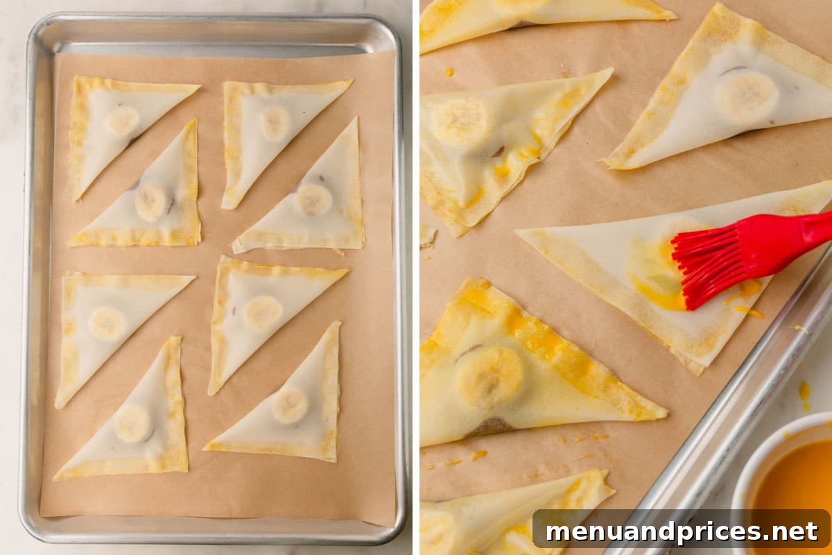 Banana Nutella wontons arranged on a parchment-lined baking sheet, being brushed with egg wash before baking.