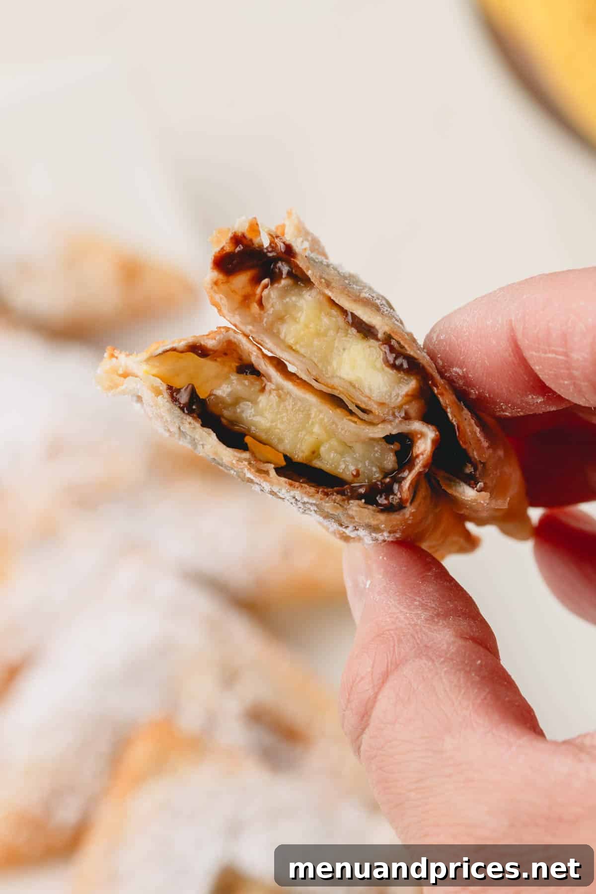 A hand holding a perfectly split banana Nutella wonton, revealing the warm, melted chocolate and tender banana filling inside.