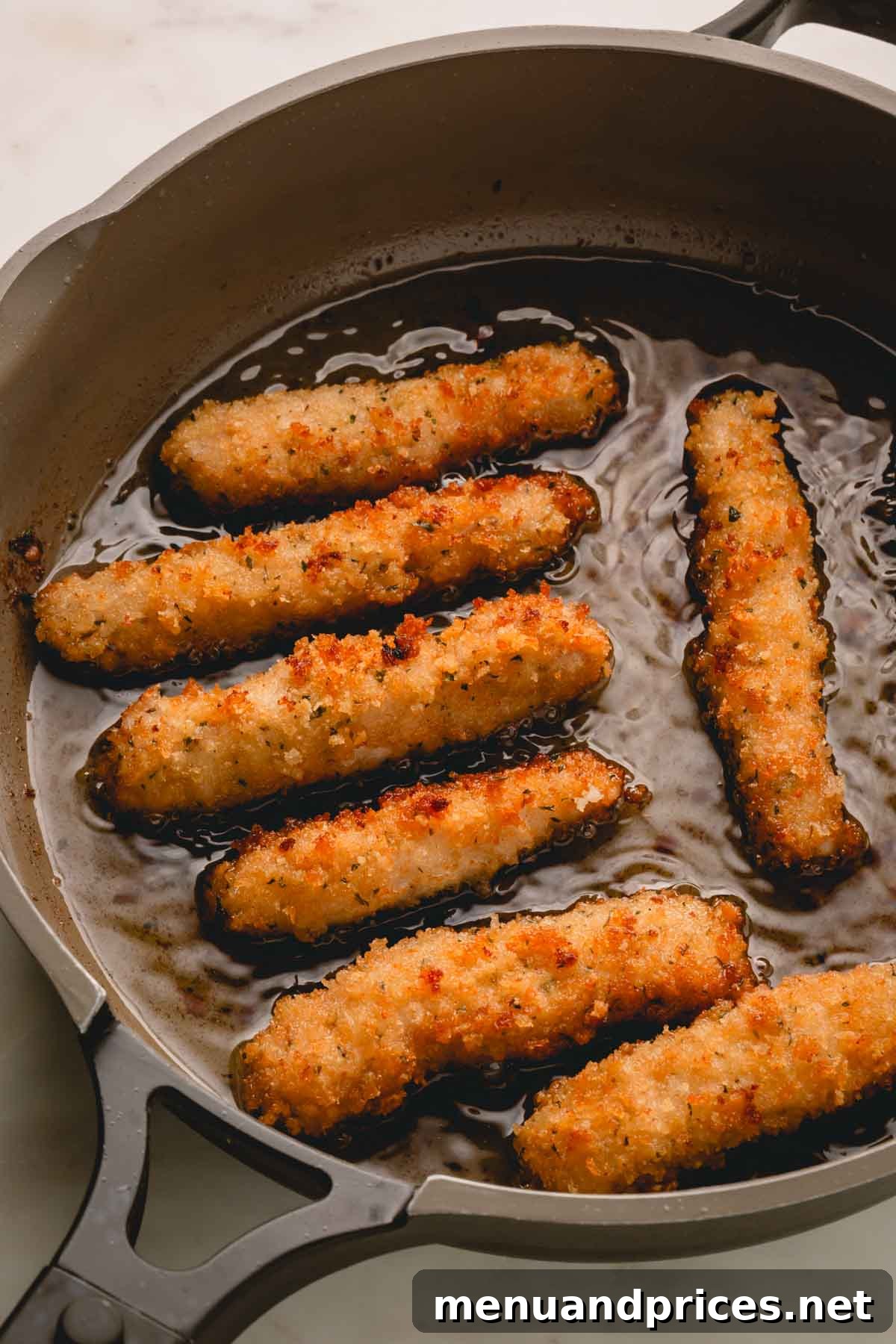 Crispy Golden Pork Strips 3 Pork strips sizzling in hot oil in a cast-iron skillet.