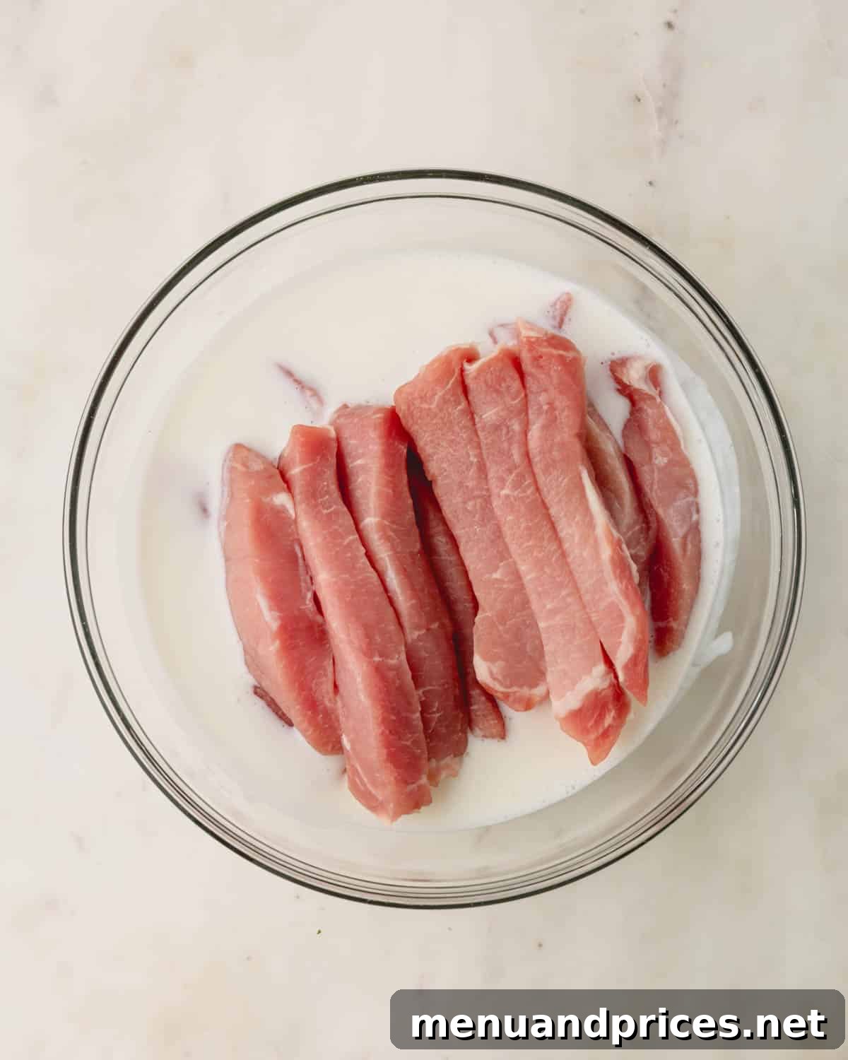 Crispy Golden Pork Strips 5 Raw strips of pork tenderloin marinating in a bowl of buttermilk for tenderness.