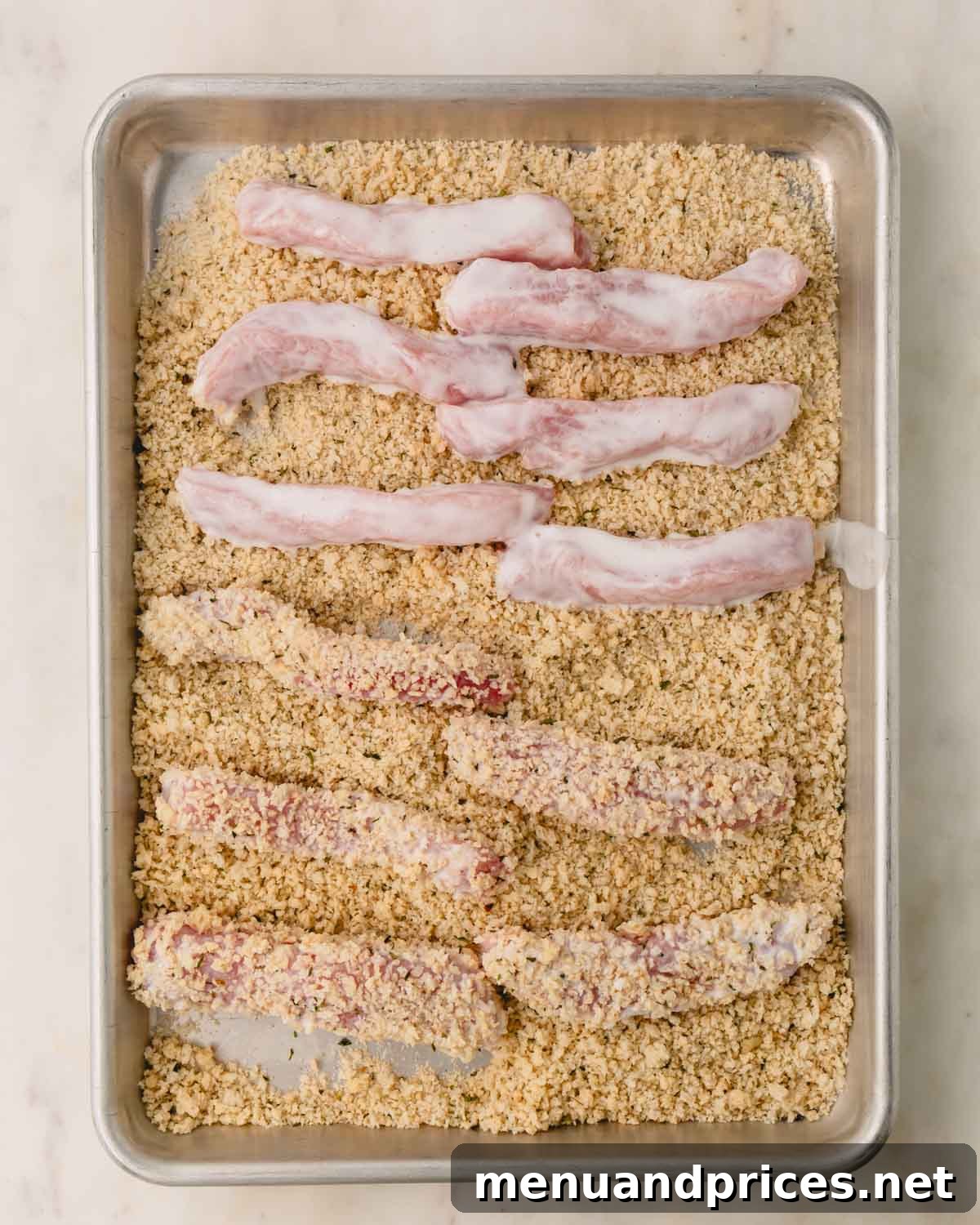 Crispy Golden Pork Strips 6 Buttermilk-coated pork strips being breaded with Panko on a baking dish.