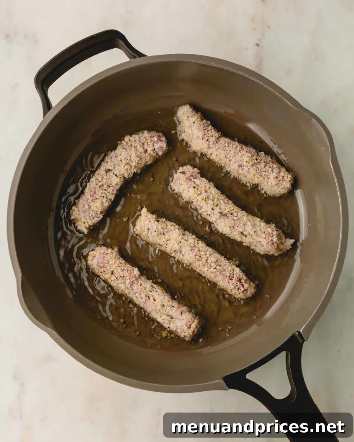 Crispy Golden Pork Strips 7 Breaded pork strips sizzling in hot oil in a skillet, turning golden.