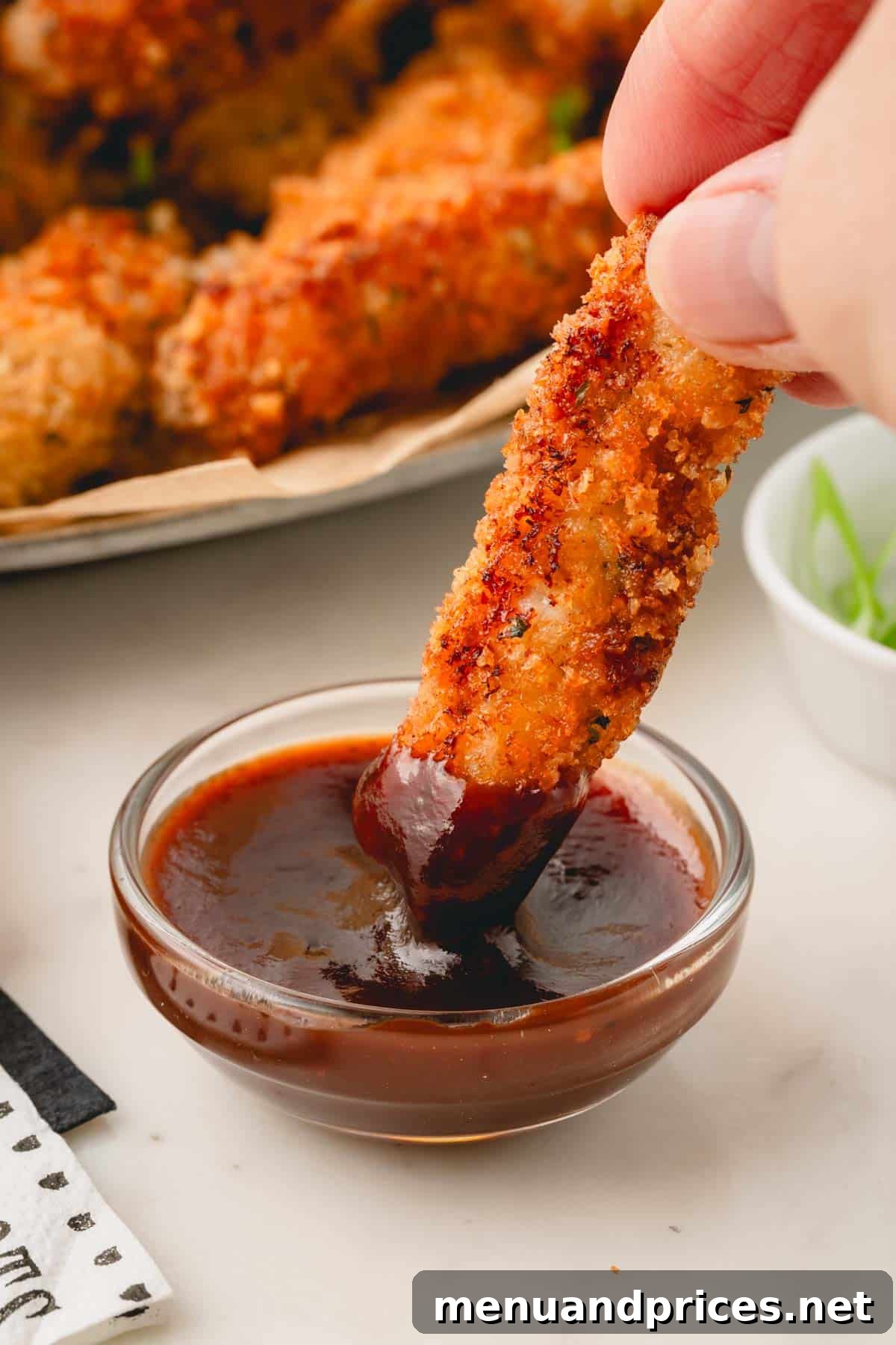 Crispy Golden Pork Strips 10 A fried pork strip being dipped into a bowl of tangy BBQ sauce.