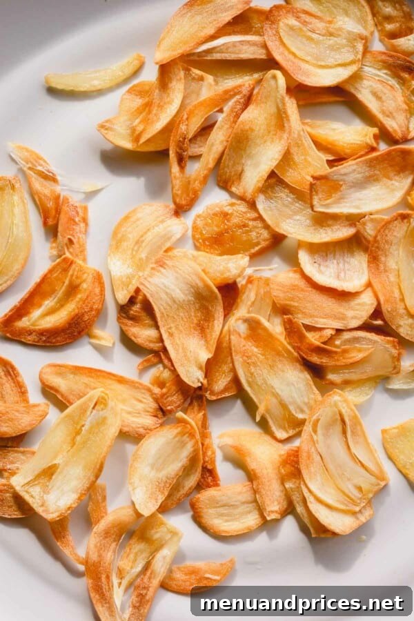 A close-up shot of perfectly golden fried garlic slices resting on a clean white plate, ready to be used as a garnish.