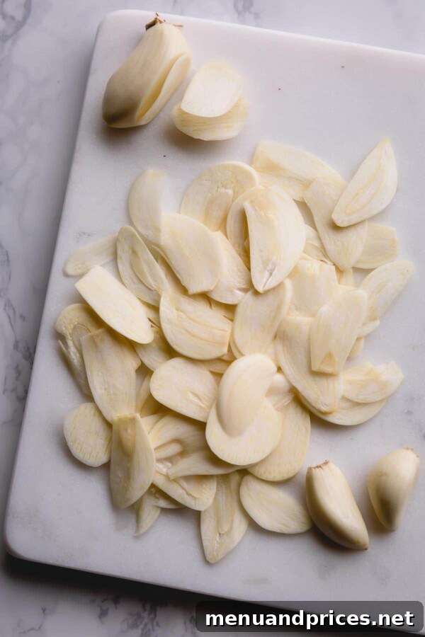 Neatly arranged, thinly sliced garlic cloves spread across a white marble cutting board, prepared for frying.