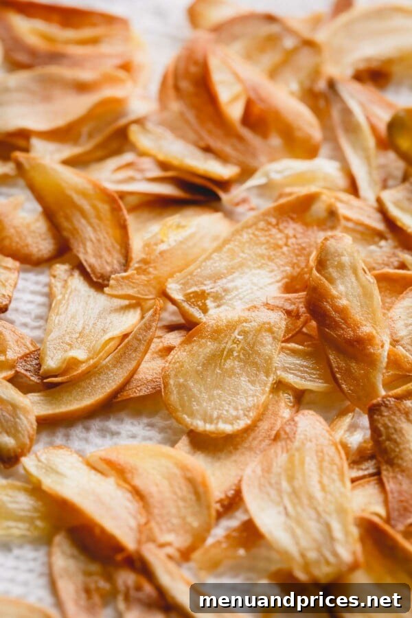An extremely close-up view of fresh fried garlic slices drying on a paper towel, highlighting their delicate, crispy texture.