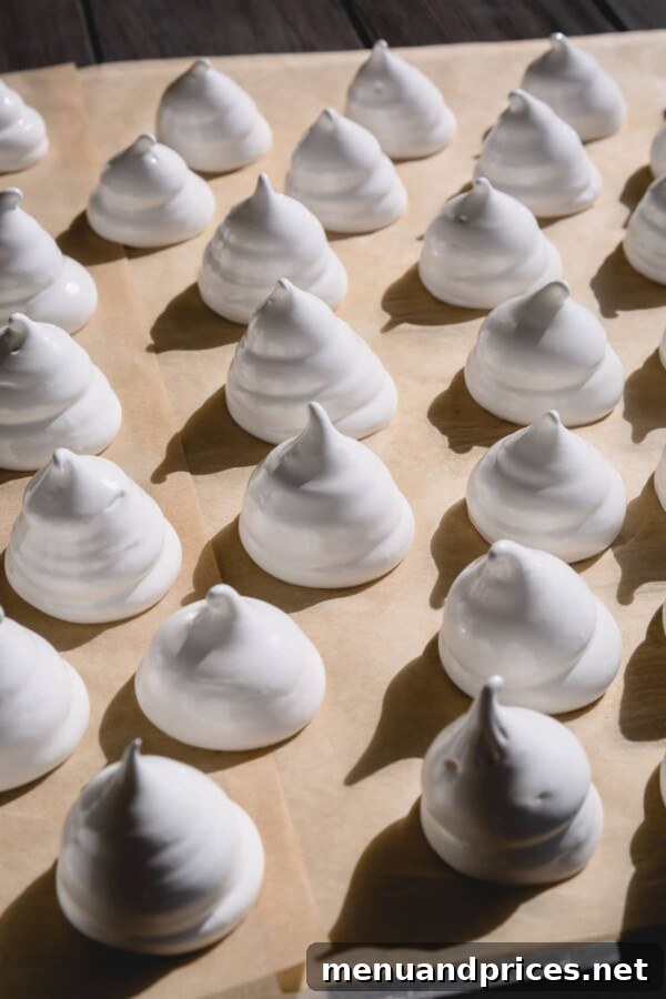 Phantom Meringue Kisses 5 A tray of freshly piped meringue ghost shapes on parchment paper, ready for the oven.
