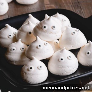 Finished meringue ghost cookies on a white plate with Halloween decorations.