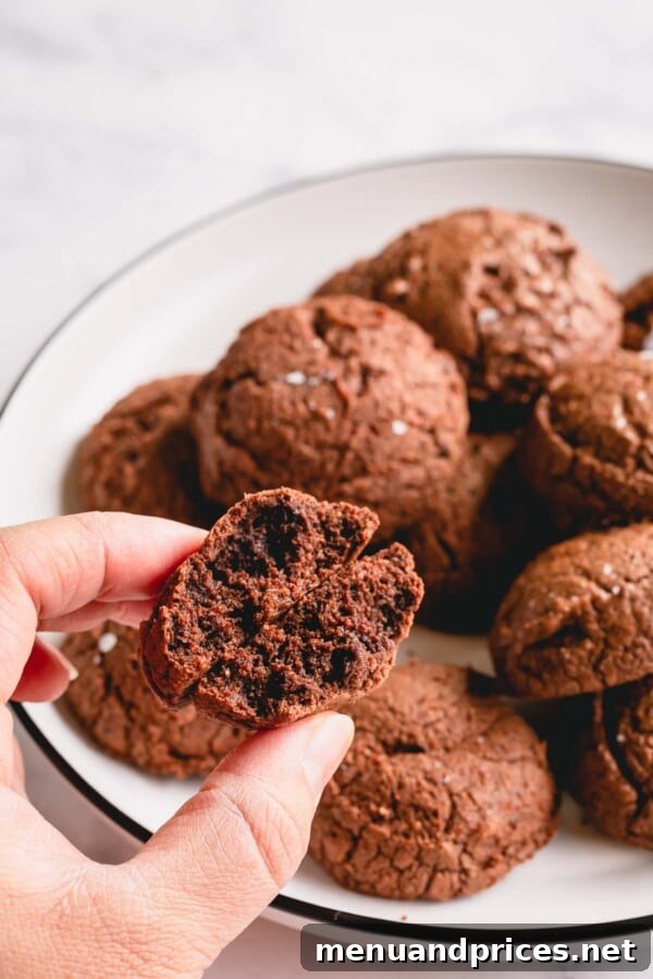 A plate of brownie cookies, with one cookie broken in half to showcase its soft, fudgy interior, emphasizing the desirable texture.