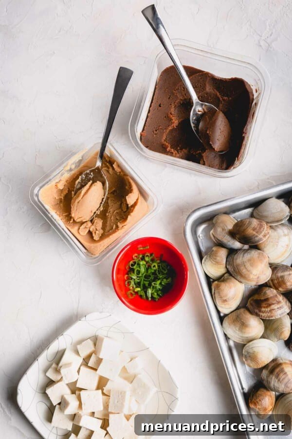 Umami Clam Miso 3 A vibrant display of fresh ingredients: red and white miso paste, plump clams, perfectly cubed tofu, and thinly sliced green onions.