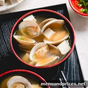 Two inviting bowls of clam miso soup presented on a black tray, garnished with fresh herbs.