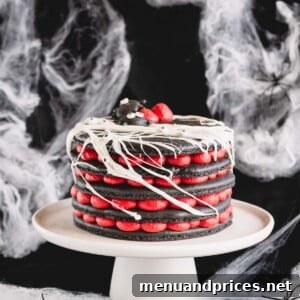 A 5-layer black macaron cake filled with red cream cheese filling, adorned with a white marshmallow spiderweb, presented on a white cake stand.
