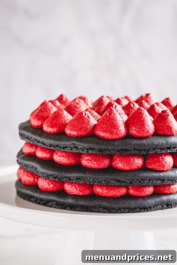 A 3-layer black macaron cake with red cream cheese filling being carefully assembled on a white cake stand, showcasing the layering process.