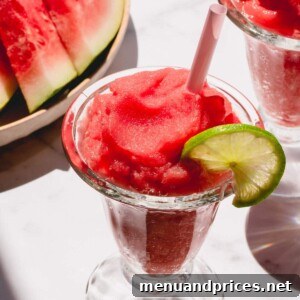 A glass of frozen watermelon daiquiri garnished with a slice of lime.