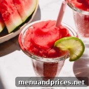 A glass of frozen watermelon daiquiri garnished with a slice of lime.