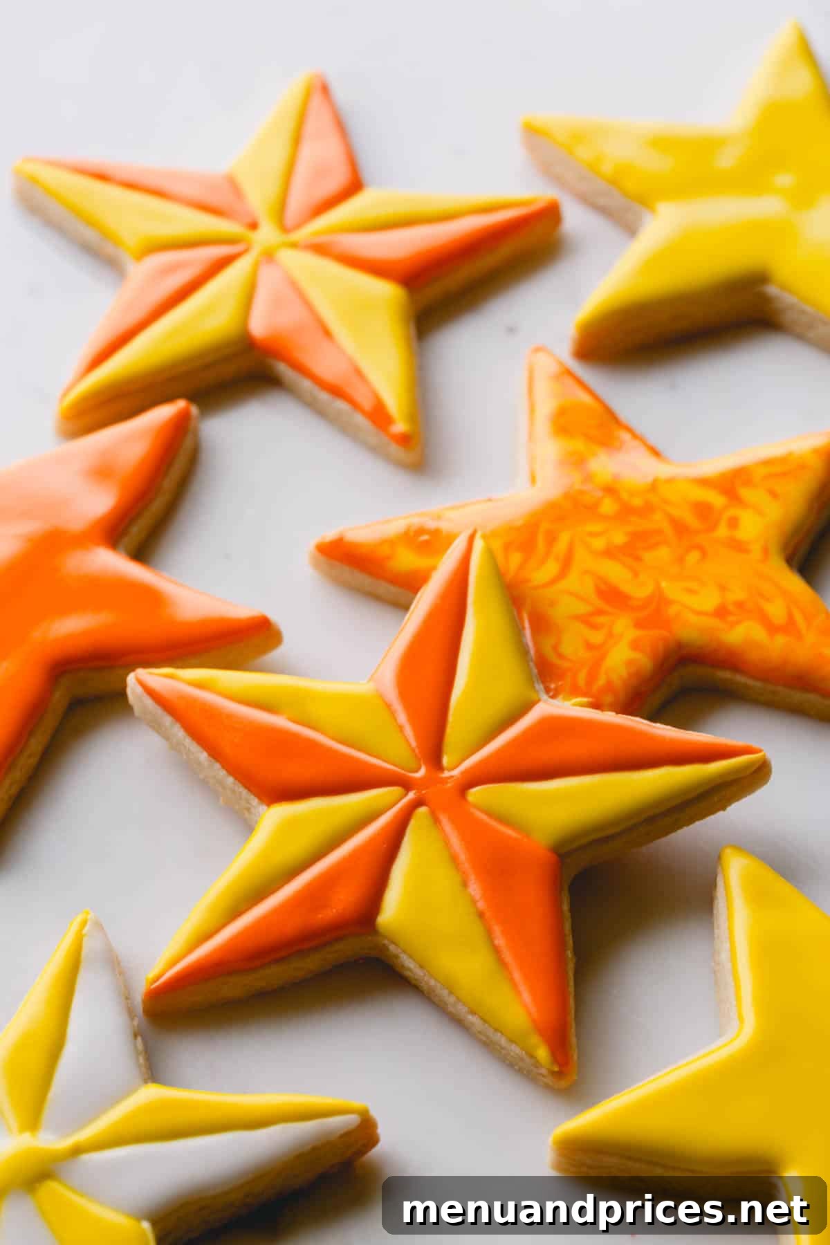 The Perfect No-Spread Sugar Cookies 3 Star shaped sugar cookies decorated with yellow and orange royal icing.