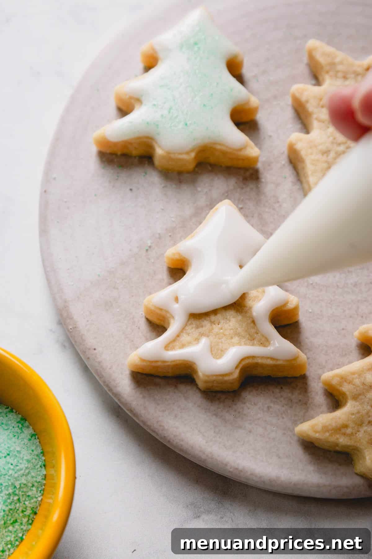 The Perfect No-Spread Sugar Cookies 9 A christmas tree shaped sugar cookie being glazed with white powdered sugar icing.