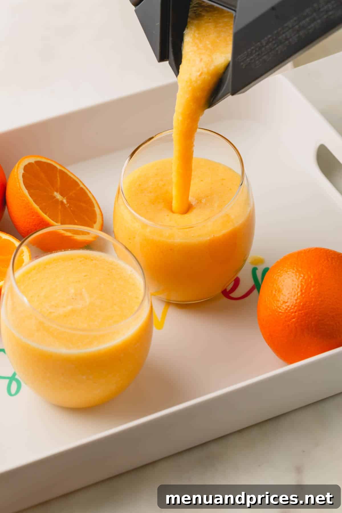 Creamy Vegan Coconut Orange Dream 6 A vibrant coconut orange Julius drink being smoothly poured from a blender into two waiting glasses, creating a frothy top.