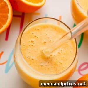A glass of coconut orange Julius with a glass straw sticking out and oranges around it.