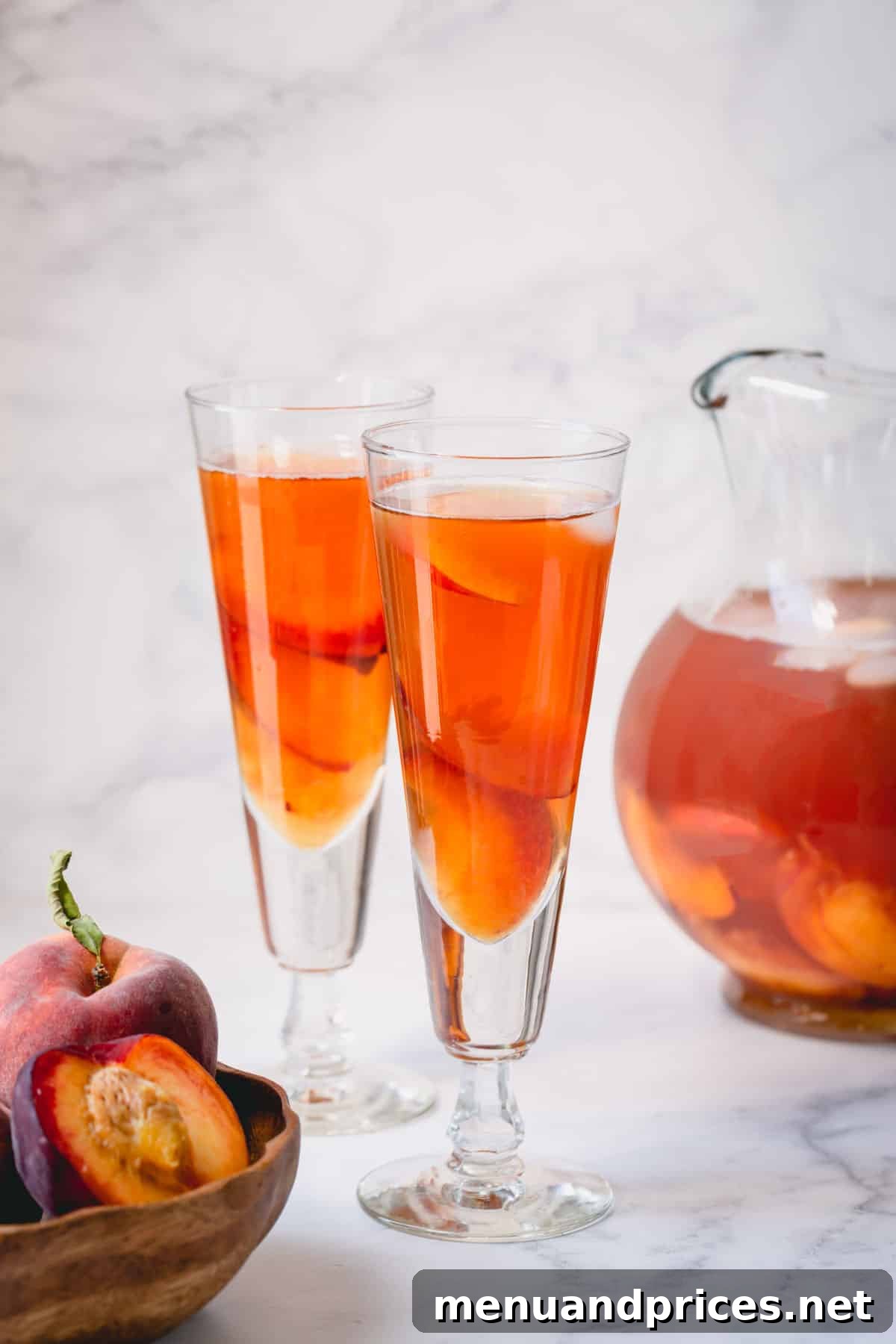 Golden Peach Chill 2 Two glasses of homemade peach iced tea, garnished with fresh peach slices and mint, on a wooden table.