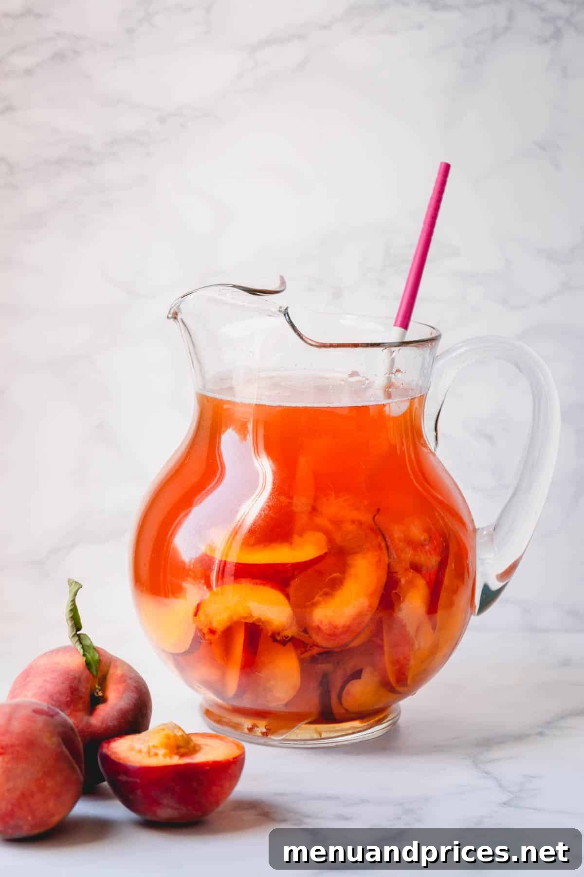 Golden Peach Chill 5 A elegant glass pitcher filled with golden peach iced tea, garnished with fresh peach slices and ice.