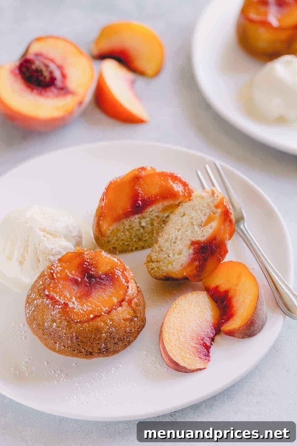 Peach upside down mini cakes on a white serving plate with vanilla ice cream and sliced peaches.