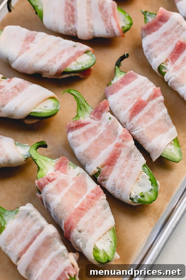 Assembled bacon-wrapped jalapeno poppers arranged on a baking sheet, ready for the oven.