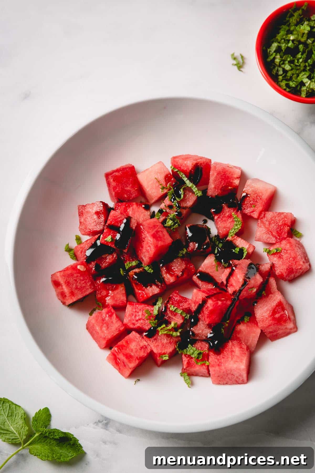 Cubed watermelon in a white bowl topped with balsamic glaze and chopped fresh mint.