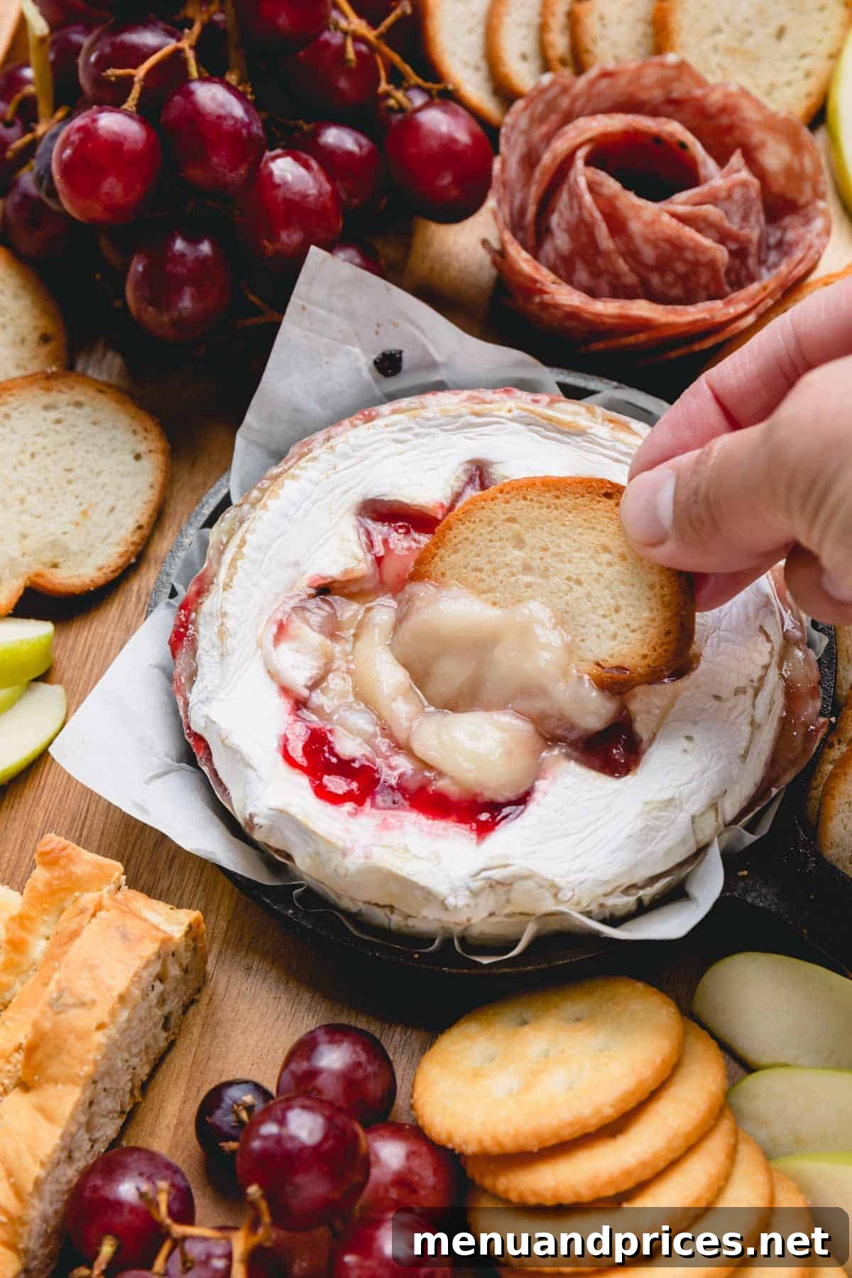 A wheel of baked raspberry Brie, with a spoon scooping out its gooey center, served with baguette chips.
