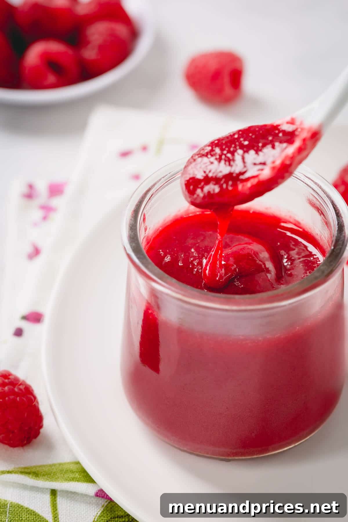 Velvety Raspberry Sauce Without the Seeds 6 Raspberry coulis elegantly stored in a clear glass jar, with a spoon gently dripping the smooth puree, highlighting its exquisite texture and rich color.