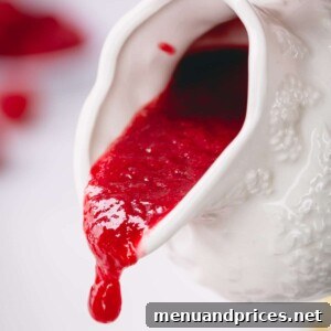 Velvety Raspberry Sauce Without the Seeds 7 A pristine white sauce pitcher pouring smooth raspberry sauce, capturing the elegance and deliciousness of the recipe.