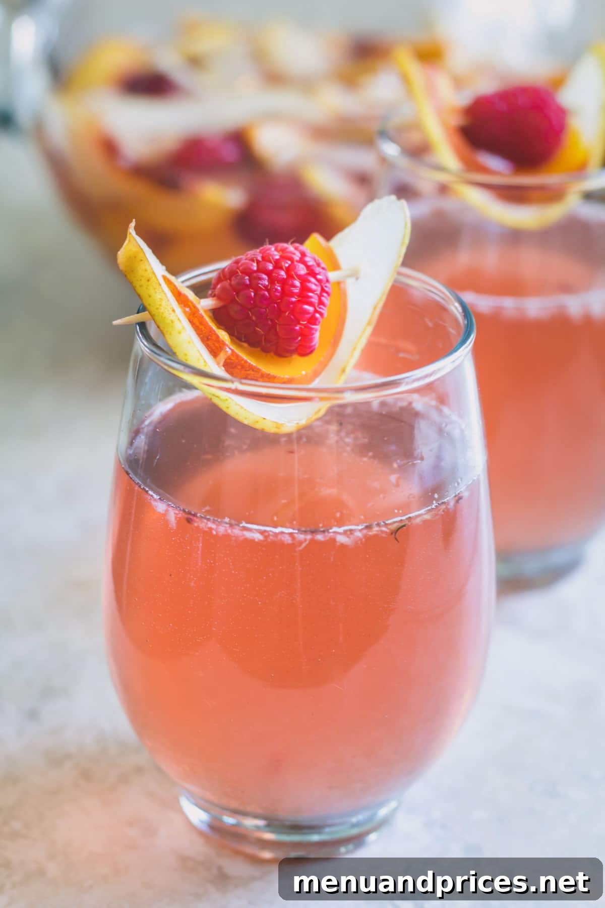 A glass of rose sangria garnished with slices of pear and peach and a raspberry.