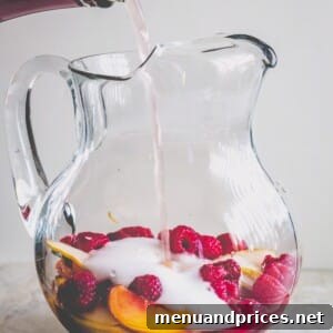 A glass pitcher filled with peach slices and raspberries and rose wine pouring in.